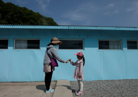 A girl and woman gesture to make a promise over a cement block symbolising a border line as they mimic a handshake between North Korean leader Kim Jong Un and South Korean President Moon Jae-in at the summit in late April, at the replica of the truce village of Panmunjom at a movie studio in Namyangju, South Korea May 8, 2018. Picture taken on May 8, 2018. REUTERS/Kwak Sung-Kyung