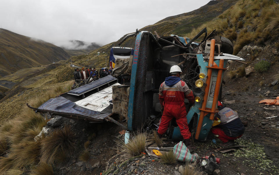 A rescue worker looks at a bus that crashed in Inca Chaca, outskirts of La Paz, Bolivia, Friday, Jan. 31, 2020. At least fourteen people died and several were injured after the bus drove off a mountain road and fell down a ravine.. (AP Photo/Juan Karita)