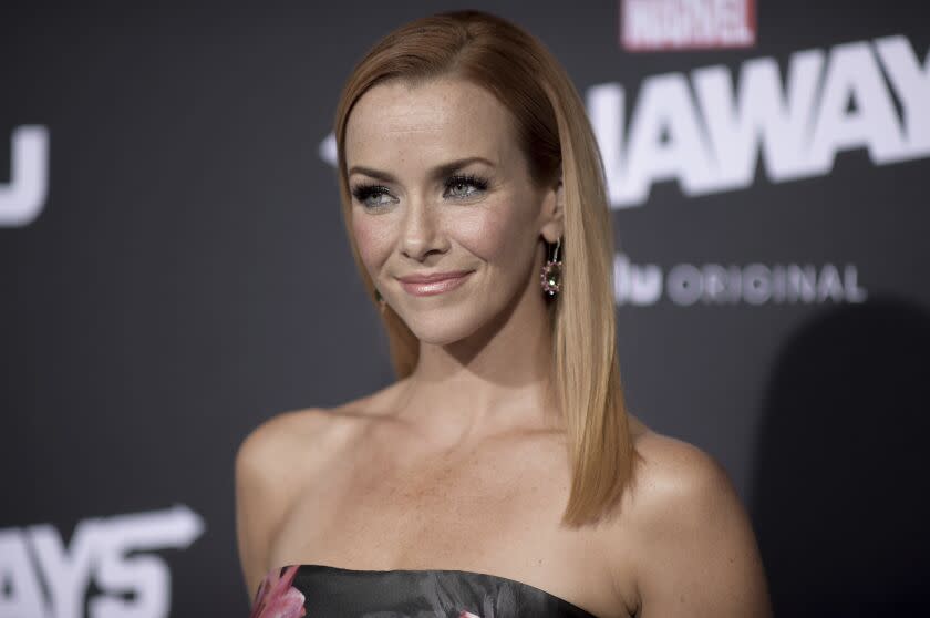 A woman with long blond hair and freckles posing in earrings and a gray dress