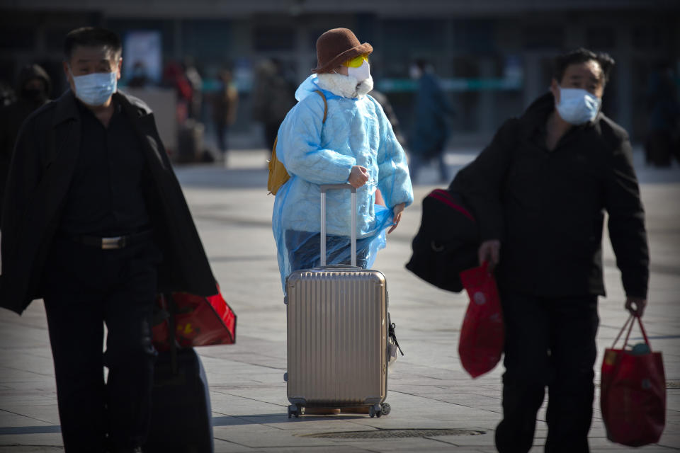 A traveler wearing face a mask, goggles, and a plastic poncho stands outside the Beijing Railway Station in Beijing, Saturday, Feb. 15, 2020. People returning to Beijing will now have to isolate themselves either at home or in a concentrated area for medical observation, said a notice from the Chinese capital's prevention and control work group published by state media late Friday. (AP Photo/Mark Schiefelbein)