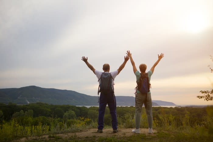 Two hikers standing at a vista with their arms outstretched above their heads