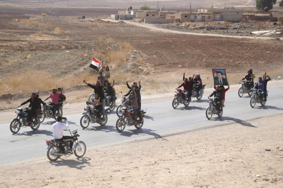 People ride motorcycles and hold a Syrian flag and a portrait of Syrian President Bashar Assad as they welcome Syrian troops as they enter the village of Ghebesh, west of the town of Tal Tamr, in northern Syria, Monday, Oct 14, 2019. Syrian government troops moved into towns and villages in northern Syria on Monday, setting up a potential clash with Turkish-led forces advancing in the area as long-standing alliances in the region begin to crumble following the pullback of U.S. forces. (AP Photo)