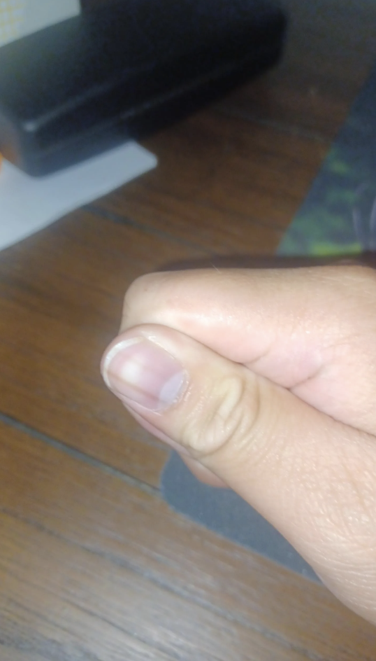 Close-up of a person's hand giving a thumbs up with a small portion of a textured wooden surface in the background