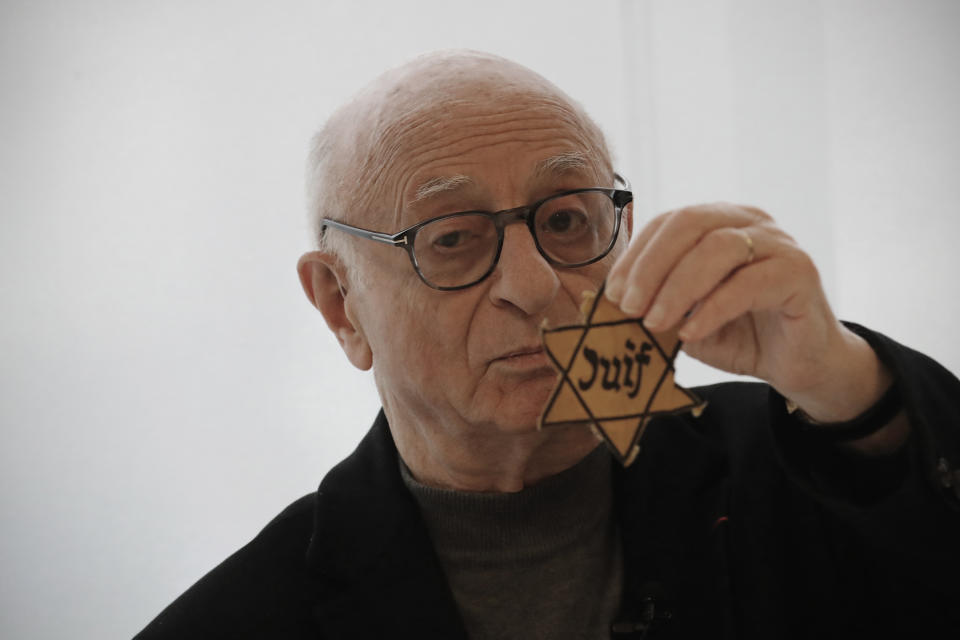 In this photo taken on Thursday Jan. 30, 2020, Victor Perahia, interned as a child in the Drancy camp and deported to Bergen-Belsen shows a Jewish badge as he speaks to students during a workshop dedicated to the Holocaust remembrance at the Drancy Shoah memorial, outside Paris. French Holocaust survivor Victor Perahia was 9 when his family was seized by the Nazis, but couldn't bear to speak about what happened for 40-years, but is now telling his story to schoolchildren at Drancy, backdropped by the buildings that once imprisoned him. (AP Photo/Christophe Ena)