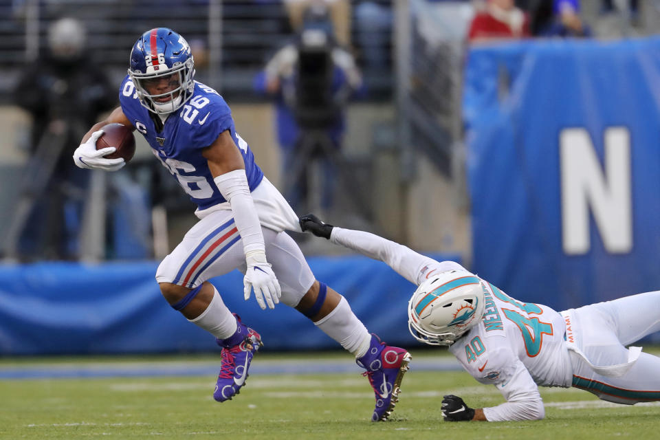 New York Giants running back Saquon Barkley (26) runs with the ball as Miami Dolphins defensive back Nik Needham (40) holds on in the second half of an NFL football game, Sunday, Dec. 15, 2019, in East Rutherford, N.J. (AP Photo/Adam Hunger)