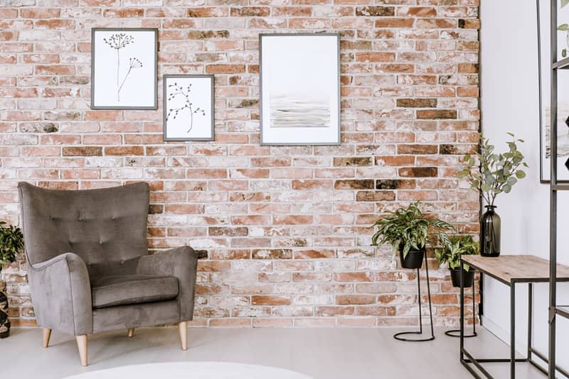 Living room interior with grey armchair, plants and posters on a red brick wall