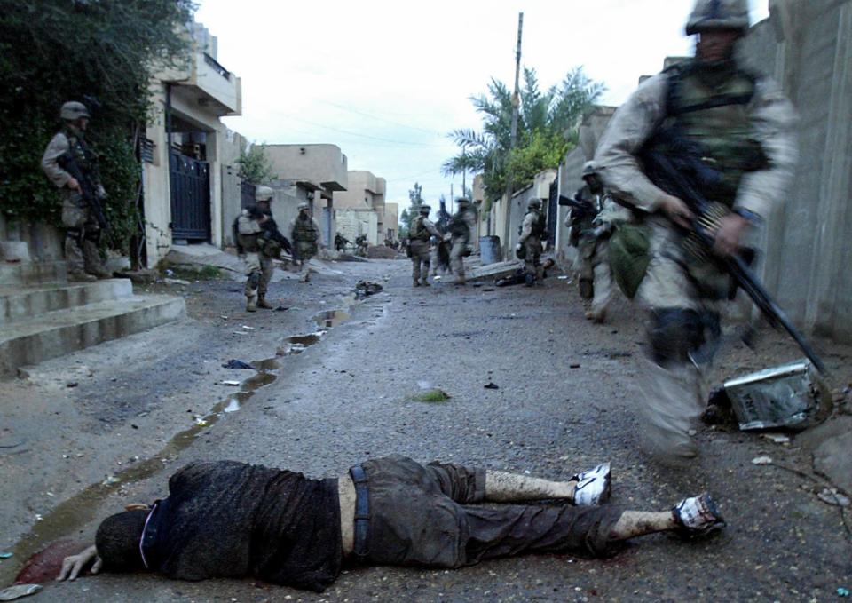 A dead man lies in the road as Marines walk past the body