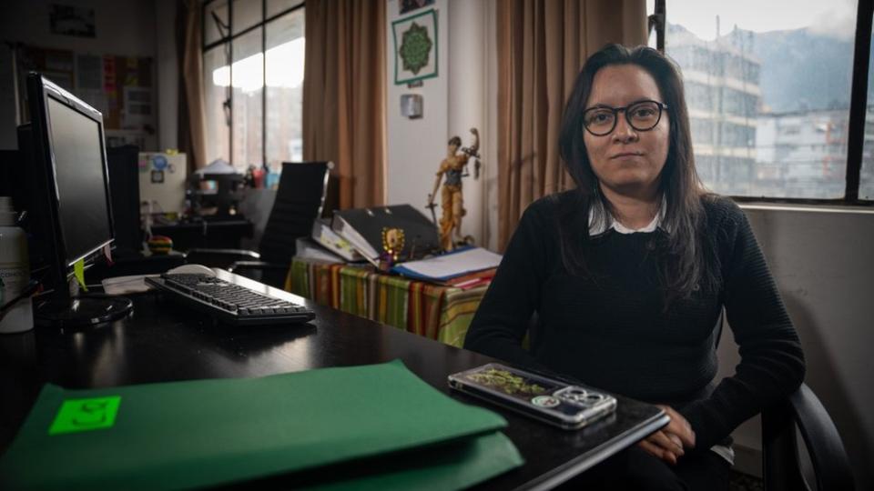 A woman in glasses sits at a desk