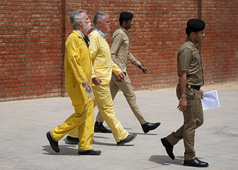 Jim Fitton of Britain, left, and Volker Waldmann of Germany, second left, wearing yellow detainees’ uniforms and handcuffed are escorted by Iraqi security forces, outside a courtroom, in Baghdad, Iraq, Sunday, May 22, 2022. Waldmann and Fitton have been accused of smuggling ancient shards out of Iraq. (AP Photo/Hadi Mizban)