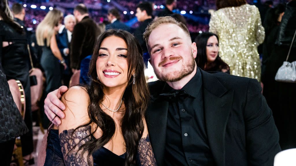 zach bryan with his arm around girlfriend brianna lapaglia and both smiling for a picture