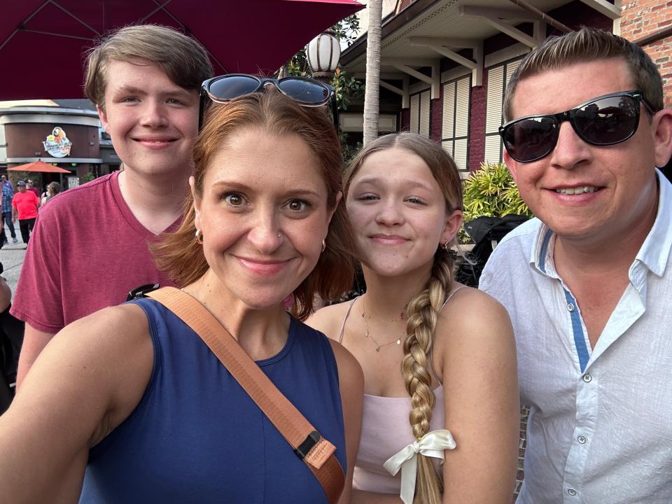 Selfie of the writer's family in front of STK Steakhouse. The writer wears a blue shirt, her son wears a red shirt, her daughter wears a pink tank top, and her husband wears sunglasses and a light-blue button-down shirt