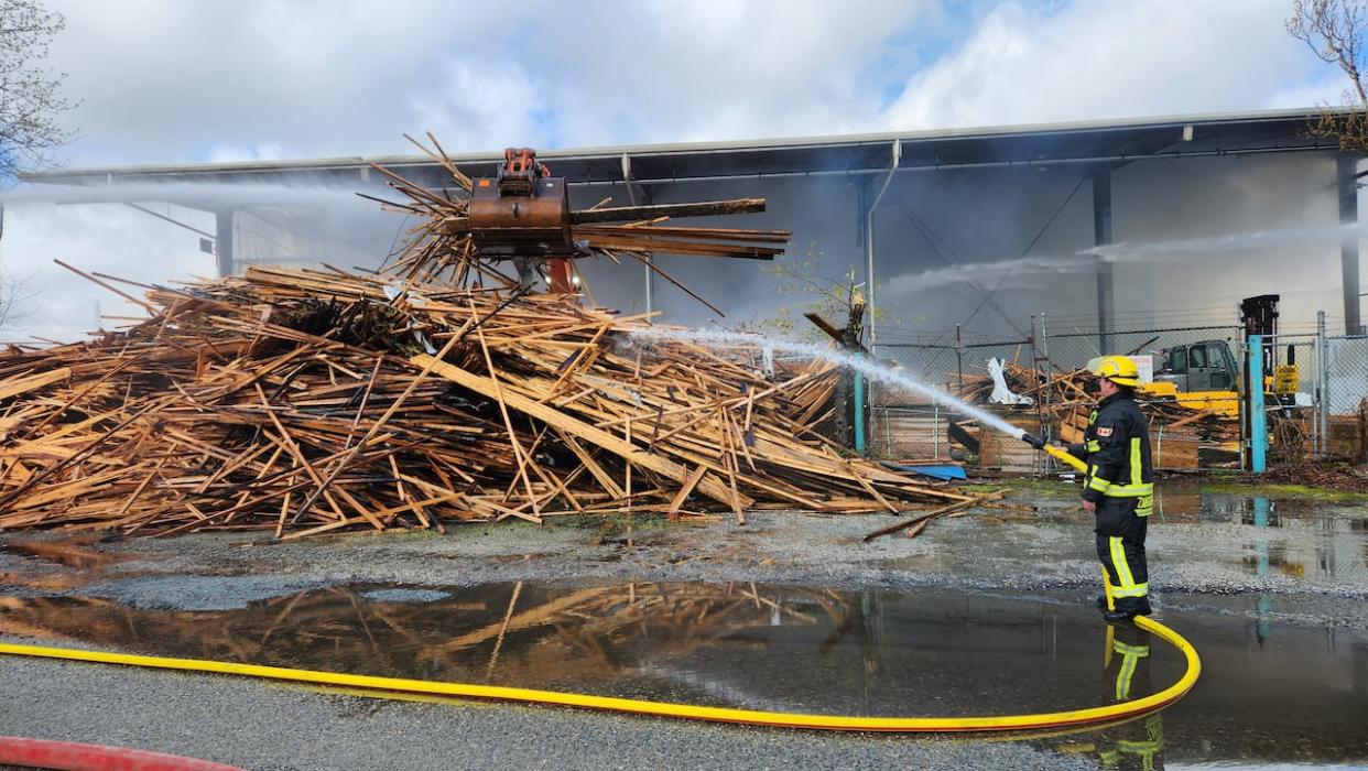 A firefighter is seen extinguishing a blaze at a lumber mill near the Fraser Surrey docks in Delta, B.C., on Sunday. (Cory Correia/CBC - image credit)
