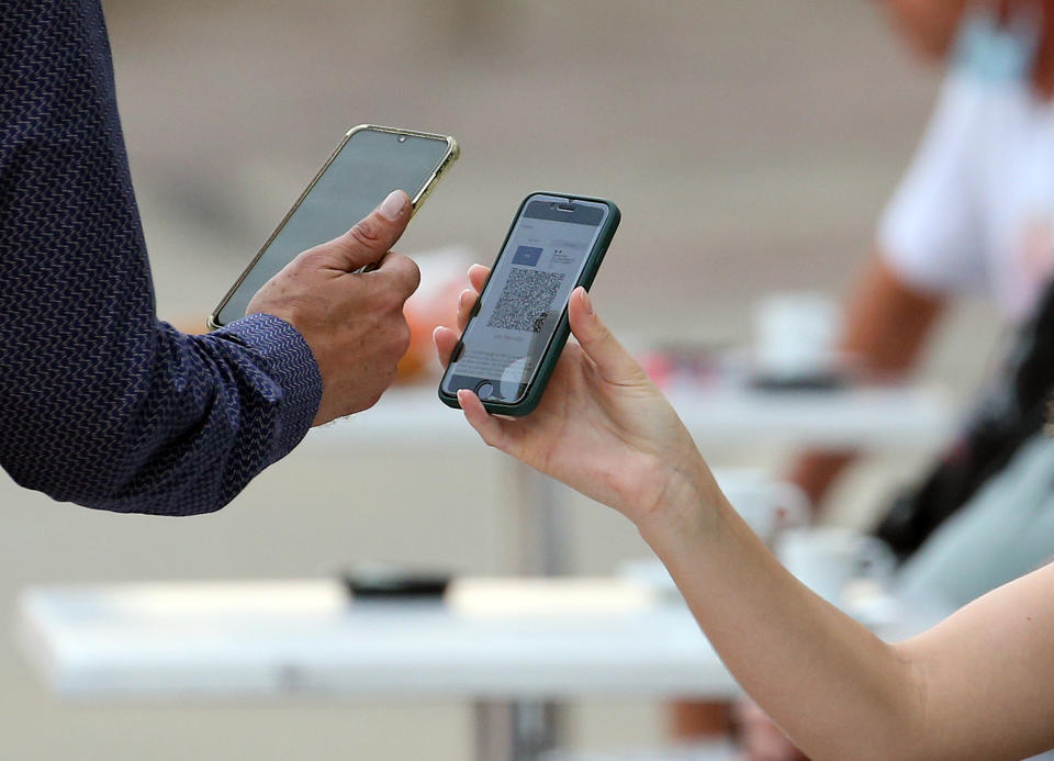 A waiter checks clients' health passes at a restaurant in Ascain, southwestern France, Wednesday, Aug. 11, 2021. People in France are now required to show a QR code proving they have a special virus pass to enjoy restaurants and cafes or travel across the country. (AP Photo/Bob Edme)