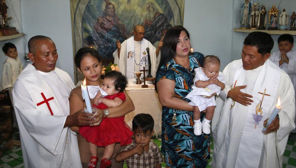 Renegade Roman Catholic priests Fr Elmer Cajilig (L) and Fr Hector Canto (R) hold candles as they stand next to their families during baptismal rites for their children in Lambunao, Iloilo on Panay island in central Philippines January 11, 2015. Also pictured is Fr Jess Siva (C). The three renegade priests say that they hope Pope Francis might hear their plea to make celibacy optional in the Roman Catholic priesthood, ahead of the pope's pastoral visit in the Philippines next week. REUTERS/Erik De Castro (PHILIPPINES - Tags: RELIGION SOCIETY)