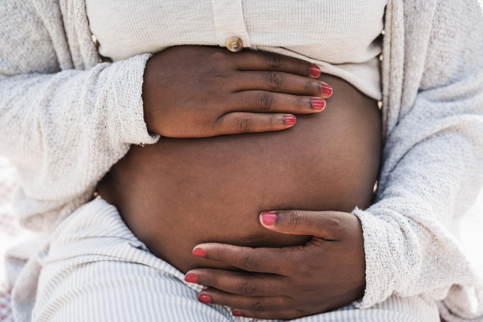 Pregnant person cradling belly with hands, dressed in cozy knitwear