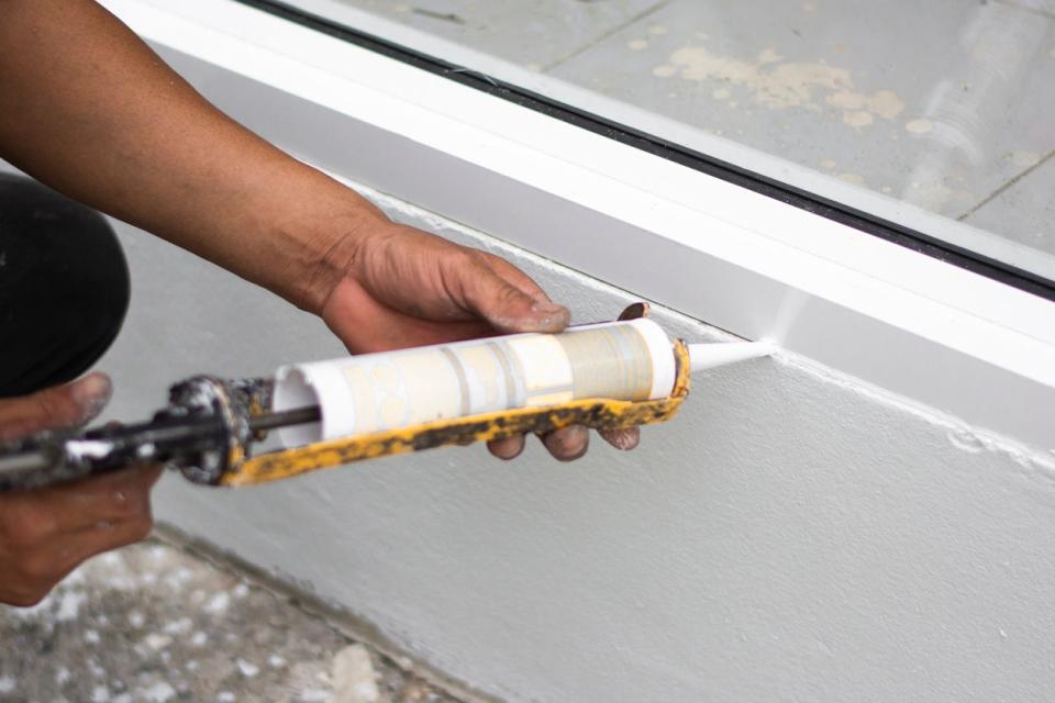 Repairman caulking a window with silicone caulk.