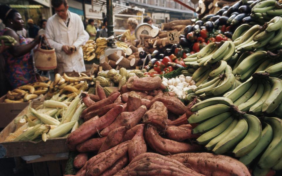 Customers weigh up the bananas, sweet potatoes or yams and peppers on sale on a fruit and vegetable market stall, Brixton, London, England circa 1969. (Photo by RDImages/Epics/Getty Images)  - Getty