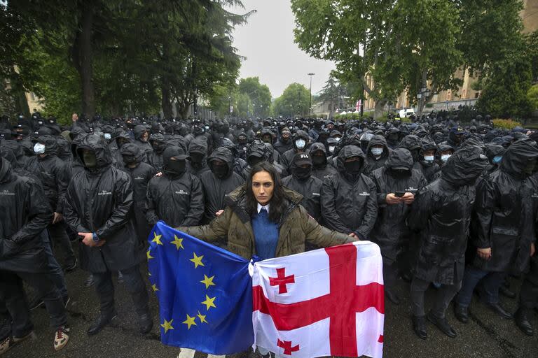 Una mujer sostiene las banderas de Georgia y la Unión Europea frente a policías antidisturbios que intentan impedir una marcha