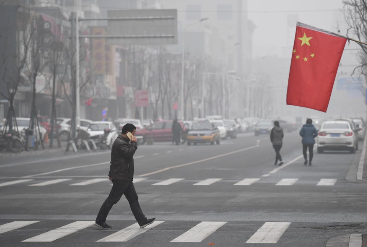 Un homme traverse une route sous le drapeau national chinois lors d'une journée très polluée à Shijiazhuang, dans la province du Hebei, dans le nord de la Chine, le 21 décembre 2016. - Greg Baker - AFP