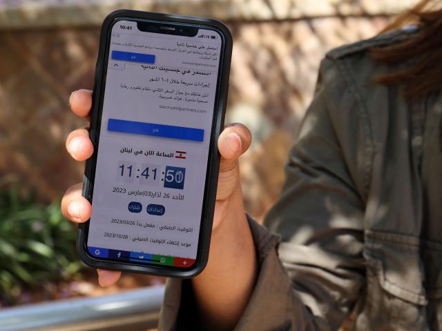 A woman in Beirut holds a mobile telephone showing contradicting time zones on March 26, 2023, after Lebanon's government announced a decision to delay daylight saving
