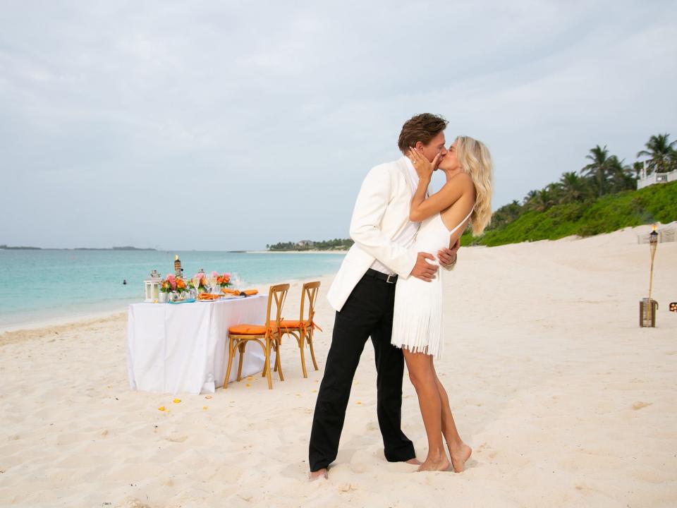 A man and a woman kiss on a beach.