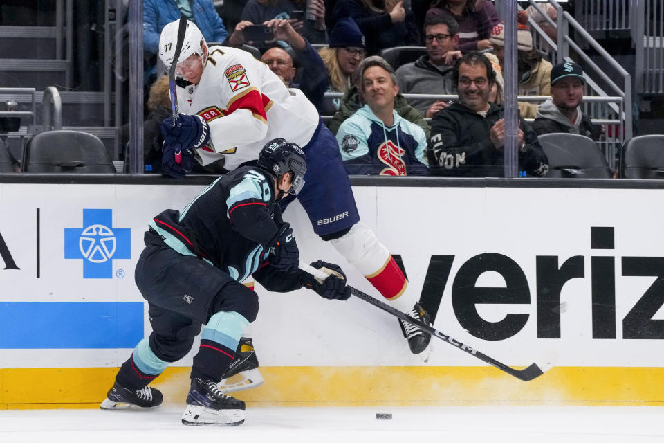 Florida Panthers defenseman Niko Mikkola (77) hits the boards as he collides with Seattle Kraken right wing Eeli Tolvanen, front, during the first period of an NHL hockey game Tuesday, Dec. 12, 2023, in Seattle. (AP Photo/Lindsey Wasson)