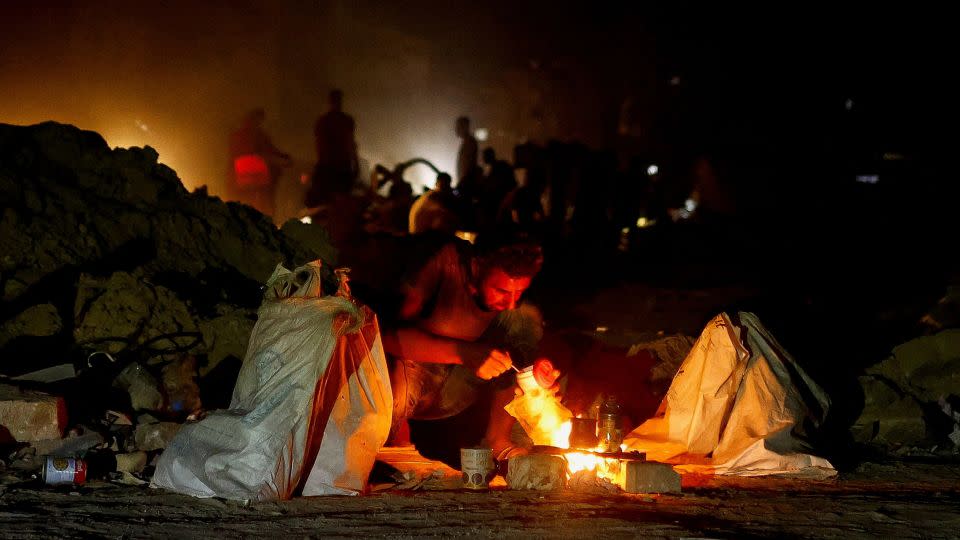 A man squats next to a fire, as Palestinians flee the eastern part of Khan Younis, after orders by Israeli army to evacuate their neighborhoods, in Khan Younis, in the southern Gaza Strip, on July 22, 2024. - Mohammed Salem/Reuters