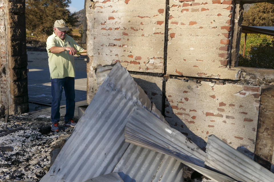 In this Tuesday, Nov. 5, 2019, photo, Ken Wilson, owner of the Soda Rock Winery, measures the old stone facade of the winery's main building in Healdsburg, Calif. The building, destroyed by the Kincade wildfire, was originally a general store and post office, built in 1869. After the fire, Soda Rock owner Ken Wilson determined to save it and reinforce it to withstand earthquakes. Signs on the nearby roadside announced wine tastings: "RECOVERY BEGINS!" Many have stopped in. "This is what I call resiliency!" one customer said as he arrived. Wilson, a Canadian who moved to Sonoma County in 1979, explained that this was how he started tastings with his first winery in 1998, "a plank and two barrels and we were in business. (AP Photo/Lacy Atkins)