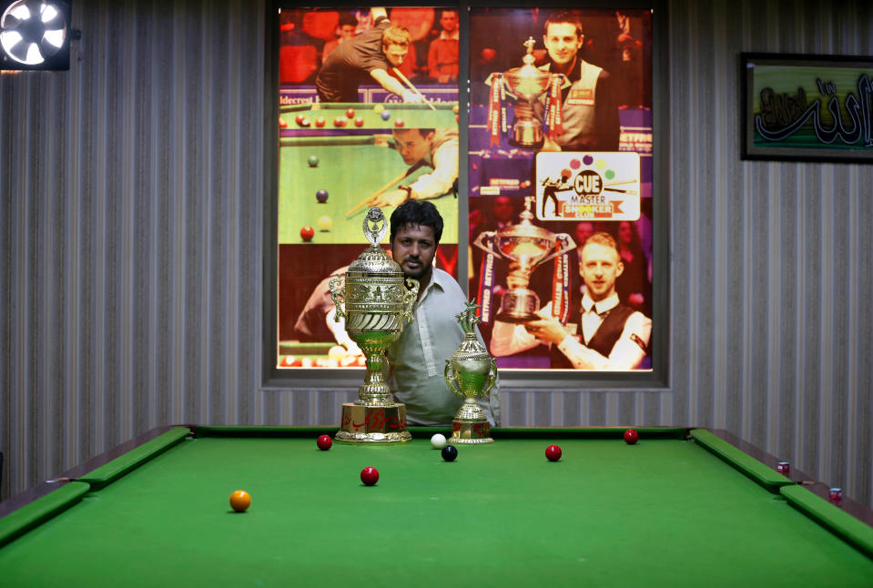 Mohammad Ikram, who play snooker with his chin, poses for photographer with his trophies at a local snooker club in Samundri town, Pakistan, Sunday, Oct. 25, 2020. Ikram, 32, was born without arms, but everyone simply admires his snooker skills when he hits the cue ball with his chin and pots a colored ball on a snooker table. He lives in a remote rural town of Punjab province and his physical disability doesn't come in his way to fulfill his childhood dream of playing the game of snooker. (AP Photo/Anjum Naveed)