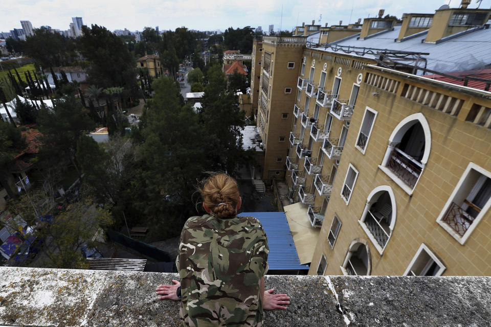 In this Friday, April 19, 2019, photo, a U.N. peacekeeper looks down at the grounds of the Ledra Palace hotel from the roof in the divided capital Nicosia, Cyprus. This grand hotel still manages to hold onto a flicker of its old majesty despite the mortal shell craters and bullet holes scarring its sandstone facade. Amid war in the summer of 1974 that cleaved Cyprus along ethnic lines, United Nations peacekeepers took over the Ledra Palace Hotel and instantly turned it into an emblem of the east Mediterranean island nation's division. (AP Photo/Petros Karadjias)