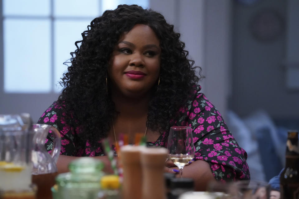 Nicole Byer sitting at a table with a glass of wine