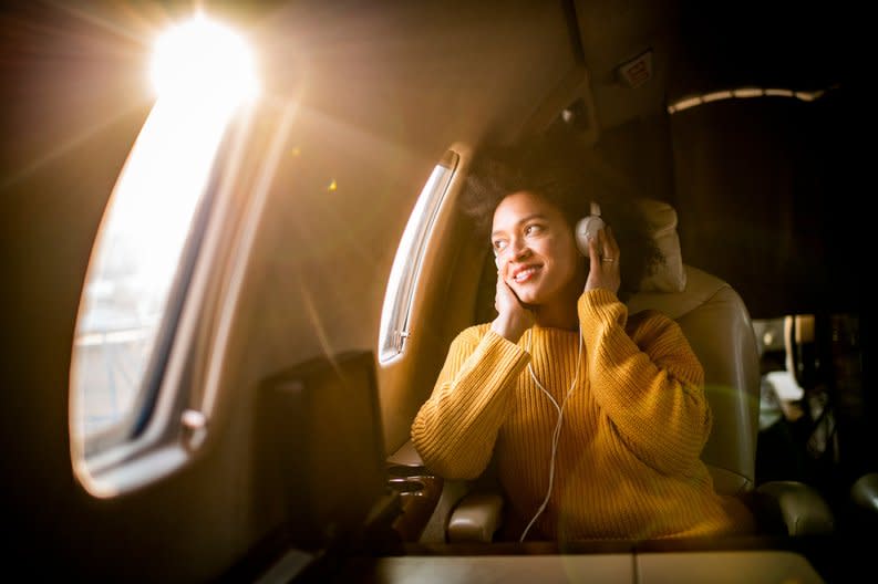 A smiling airplane passenger listening to music and looking out the window.