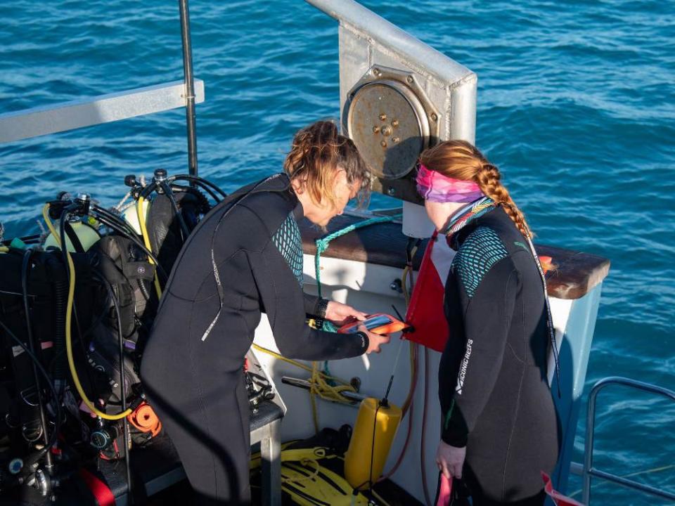 Mission: Iconic Reefs field team member Cate Gelston, co-lead scientist on the assessment cruise, and Data Manager Grace Hanson, prepare a GPS unit in advance of outplant health assessment surveys.