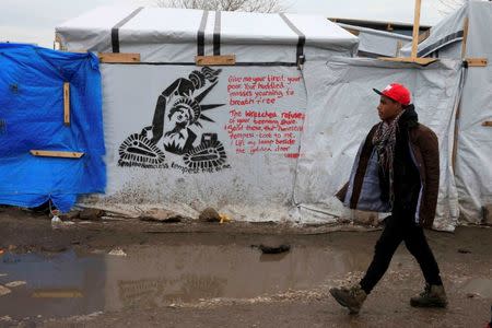 A migrant walks past a stencil graffiti with a statue of liberty and the message, "Send the Homless, Tempest tost to me", in the southern part of a camp for migrants called the "jungle", in Calais, northern France, February 23, 2016. REUTERS/Pascal Rossignol