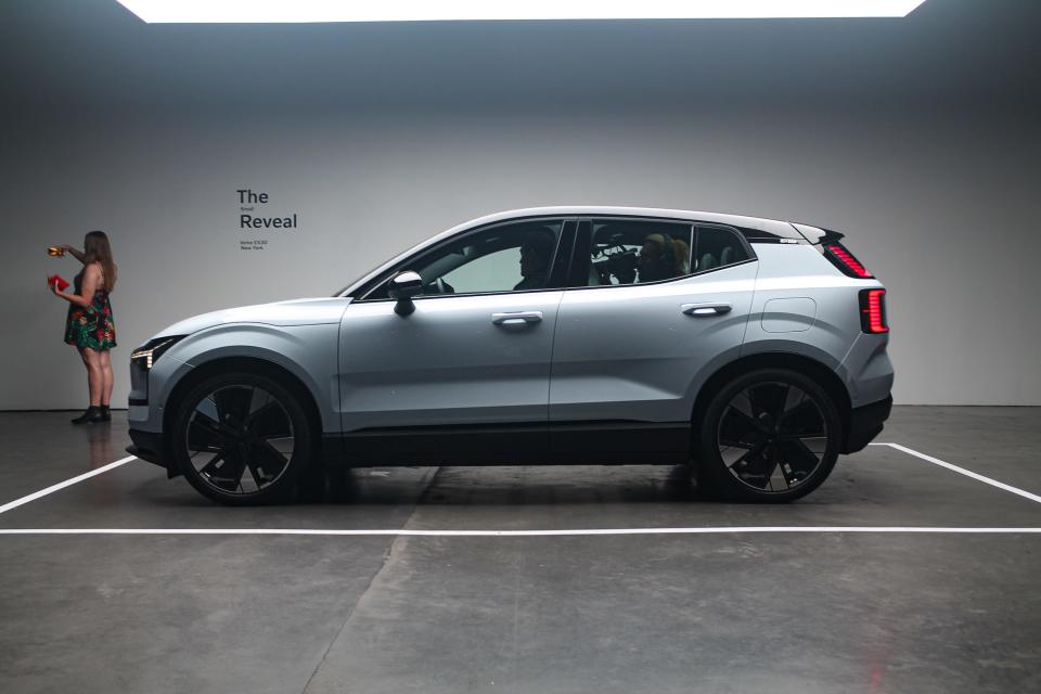 A woman standing against a wall near the Volvo EX30, which has been parked in an exhibition space marked with a white line.