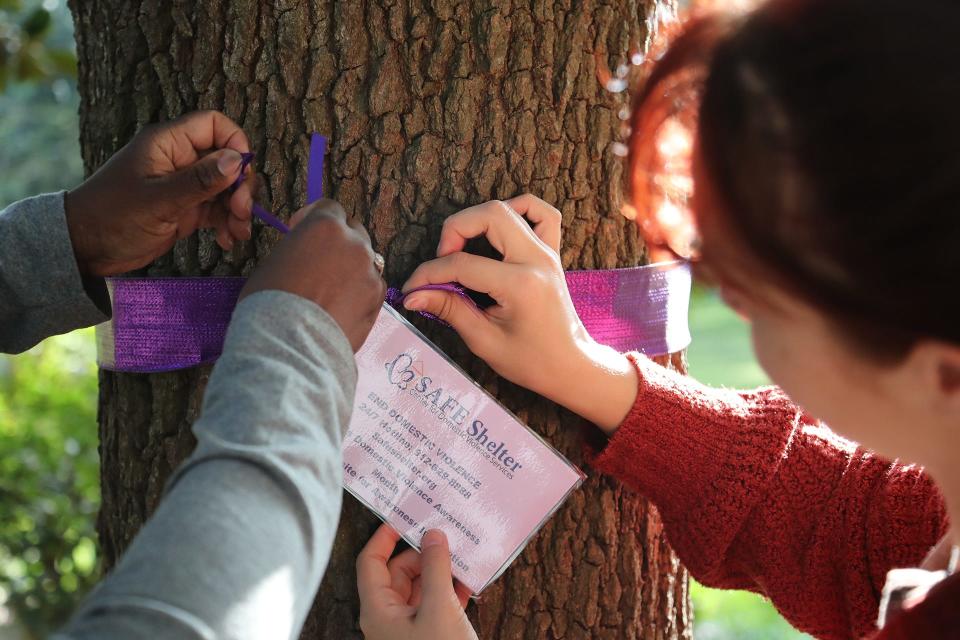 Doretha Rice, program director SAFE Shelter, and volunteer Rachel Simmons work together to tie a card with SAFE Shelter's information onto a purple ribbon around a tree in Forsyth Park on Monday, September 2, 2023 in honor of Domestic Violence Awareness Month.