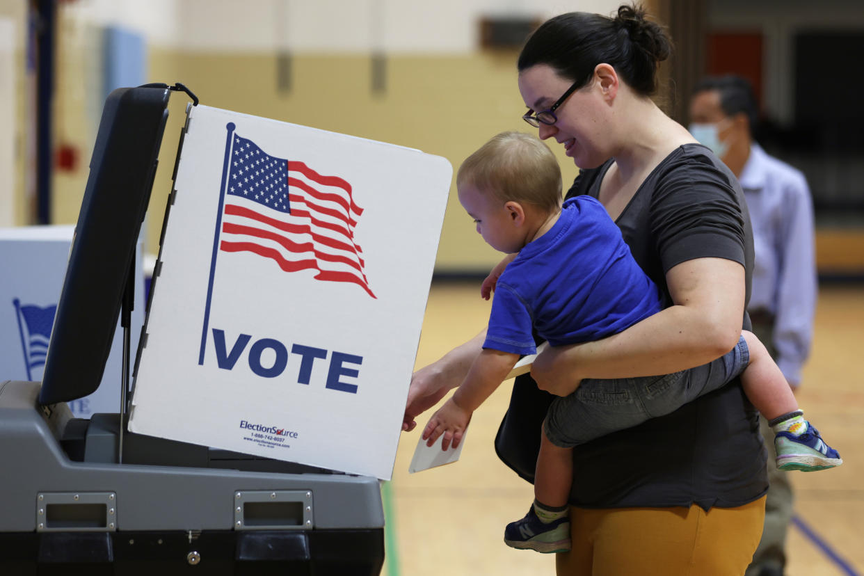 A voter holding her child casts her ballot at a polling location.