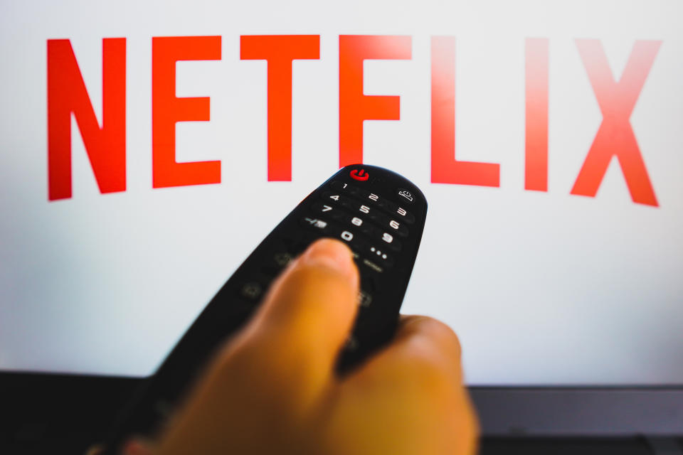 In this photo illustration, a hand holds a TV remote control in front of the Netflix logo on a TV screen.