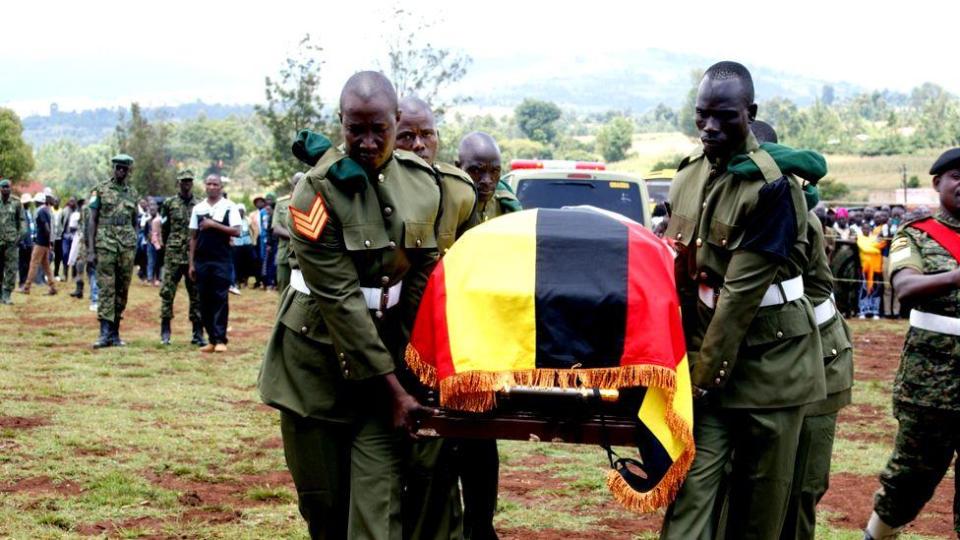 A coffin draped in a Ugandan flag being carried