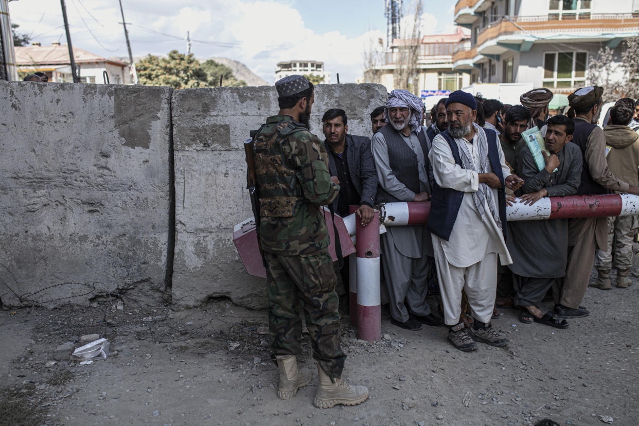 People gather outside as a Taliban fighter controls the entrance to the government passport office 