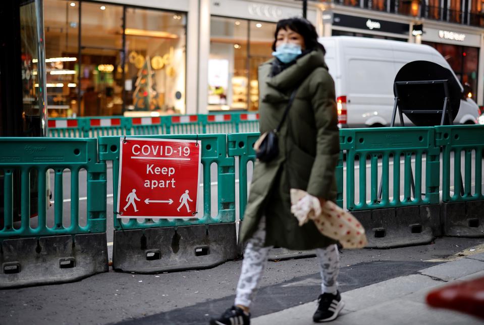 A pedestrian wearing a face mask or covering due to the COVID-19 pandemic, walks past a COVID-19 sign asking people to social distance as they walk on Oxford Street in central London on December 22, 2020. - UK government borrowing continued to soar in November on emergency action to support the virus-hit economy which nevertheless rebounded stronger than expected in the third quarter, official data showed Tuesday. Government borrowing last month hit £31.6 billion ($41.8 billion, 34.2 billion euros), a record for November -- taking public sector net debt to £2.1 trillion, the Office for National Statistics said in a statement. (Photo by Tolga Akmen / AFP) (Photo by TOLGA AKMEN/AFP via Getty Images)