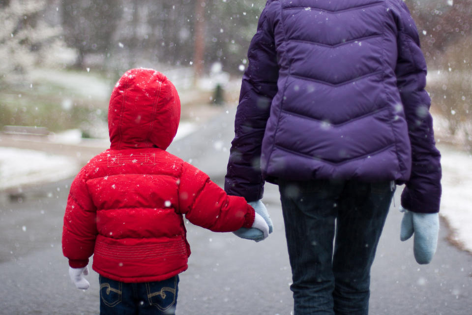 Two children dressed in coats, walking down a road with snow falling. energy bills 