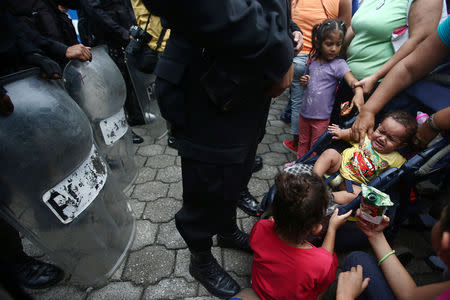 A Honduran migrant child, part of a caravan trying to reach the U.S., cries in front of a police officer line up in the checkpoint between Guatemala and Mexico in Tecun Uman, Guatemala October 19, 2018. REUTERS/Edgard Garrido
