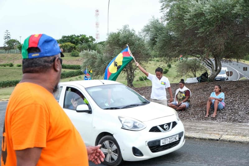 A demonstrator waves a flag of the socialist National Liberation Front of the Kanaks (FLNKS) at a vehicle checkpoint in Noumea amid protests related to a debate on a draft constitution aimed at expanding the electorate for upcoming elections in the French overseas territory of New Caledonia. More than 130 people were arrested in New Caledonia as violent protests rocked the French archipelago in the Pacific. Theo Rouby/AFP/dpa