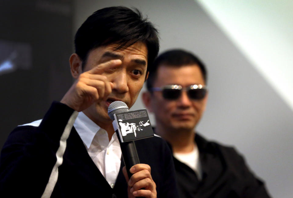 Movie director Wong Kar-wai, right, watches from the background as Tony Leung, left, speaks during a press conference on Wednesday, Jan. 23, 2013 in Singapore. For a director and actor who have worked together for about two decades, there did not seem to be much chemistry between Wong and Leung at the news conference promoting their new movie "The Grandmaster." (AP Photo/Wong Maye-E)