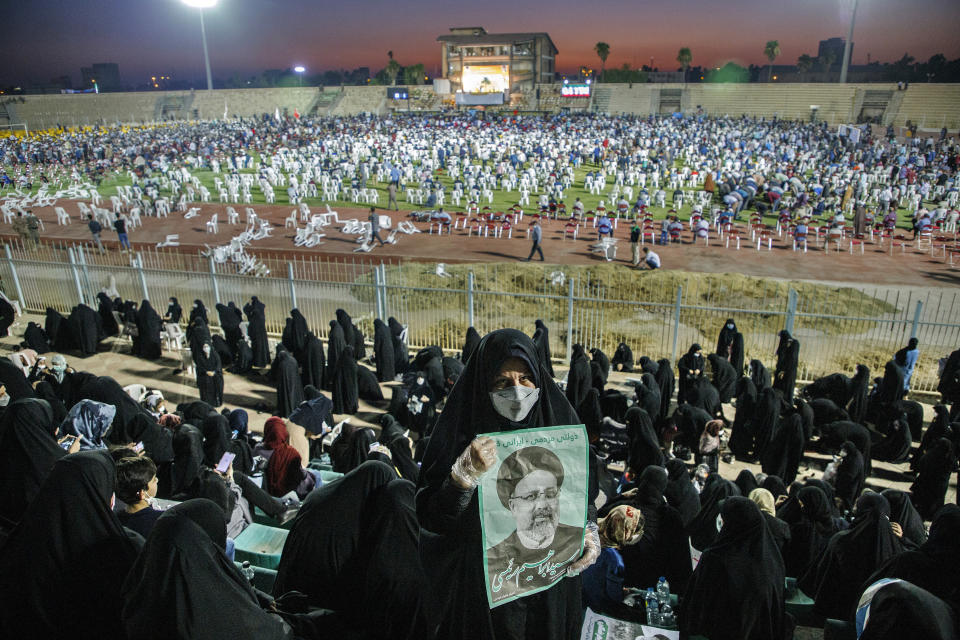 In this Wednesday, June 9, 2021, photo, a supporter of the presidential candidate Ebrahim Raisi, currently judiciary chief, hold posters of him during a campaign rally at the Takhti Stadium in Ahvaz, Iran. Around 5,000 of people have gathered in a football stadium in southeastern city of Ahvaz to support the Iranian hard-line presidential candidate, Iranian media reported. (Amin Nazari/ISNA via AP)