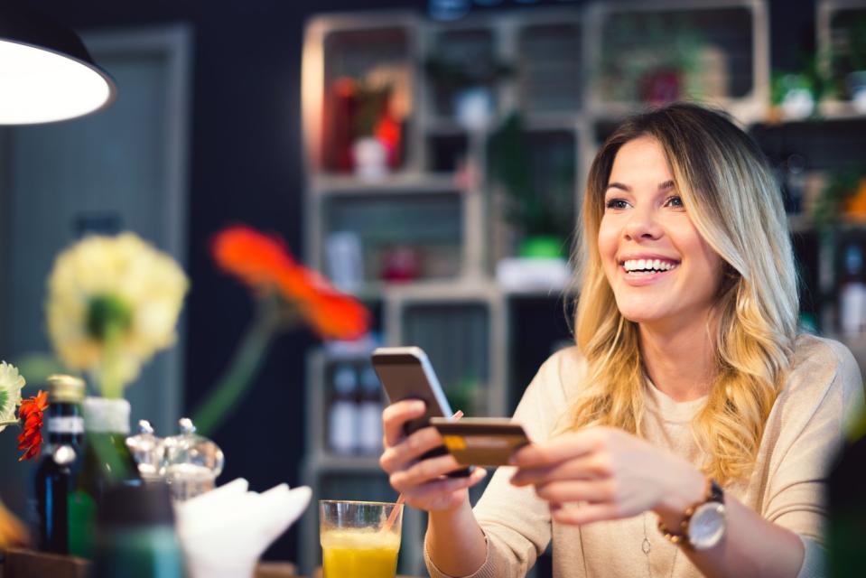 A customer at a restaurant holds a credit card and a smartphone.