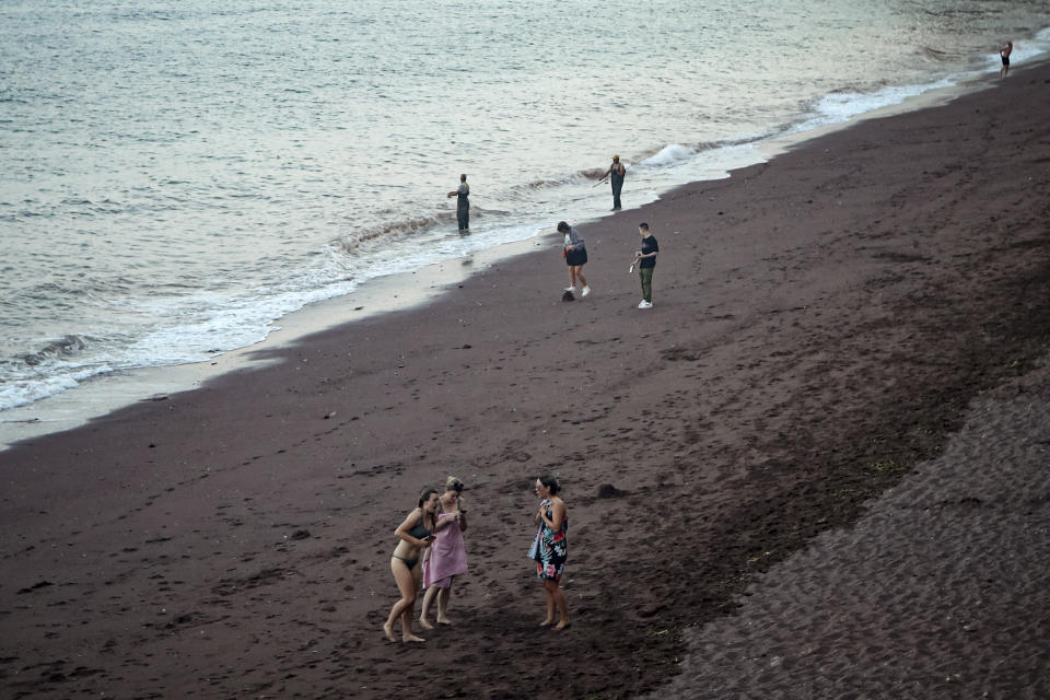 People gather on Ness Cove beach in Shaldon, Devon, England, Thursday July 22, 2021. Visiting the fishing village of Shaldon a small cluster of mainly Georgian houses and shops at the mouth of the River Teign, is like stepping back into a bygone era. It features simple pleasures that hark back to analog, unplugged summer days: a book and a picnic blanket, a bucket and spade, fish and chips. (AP Photo/Tony Hicks)