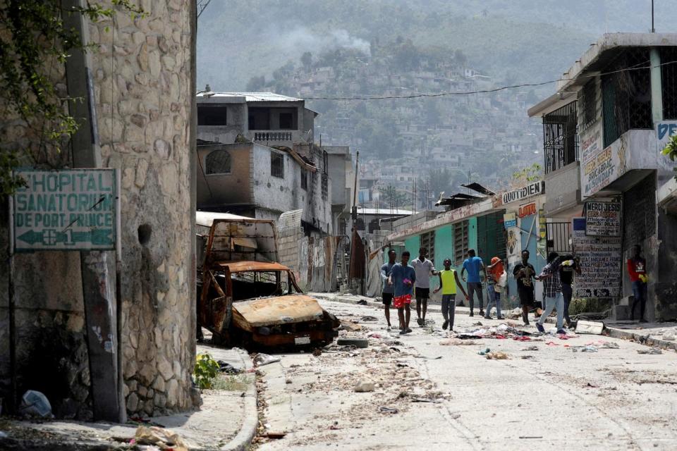 PHOTO: People walk past a damaged car in the Carrefour Feuilles neighborhood, which was deserted due to gang violence, in Port-au-Prince, Haiti, on March 19, 2024.  (Ralph Tedy Erol/Reuters)