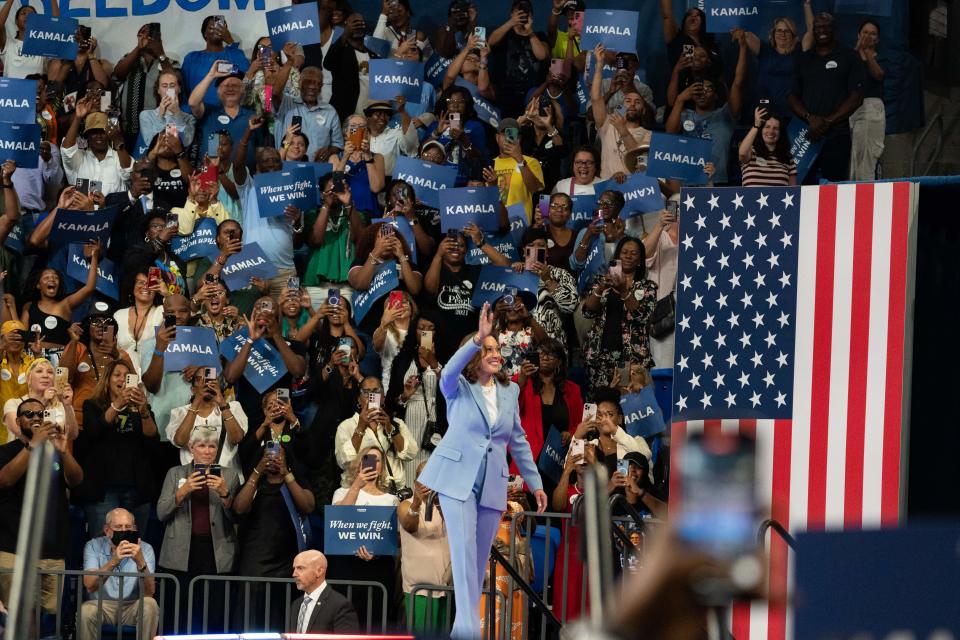 Kamala Harris waving to a crowd holding signs that say "Kalama" It is "When we fight, we win."